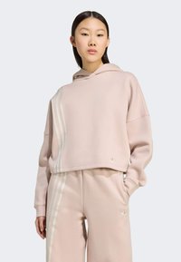 Pink cropped hoodie with a hood, featuring three white stripes on one side and a small logo on the hem. Soft texture and relaxed fit.