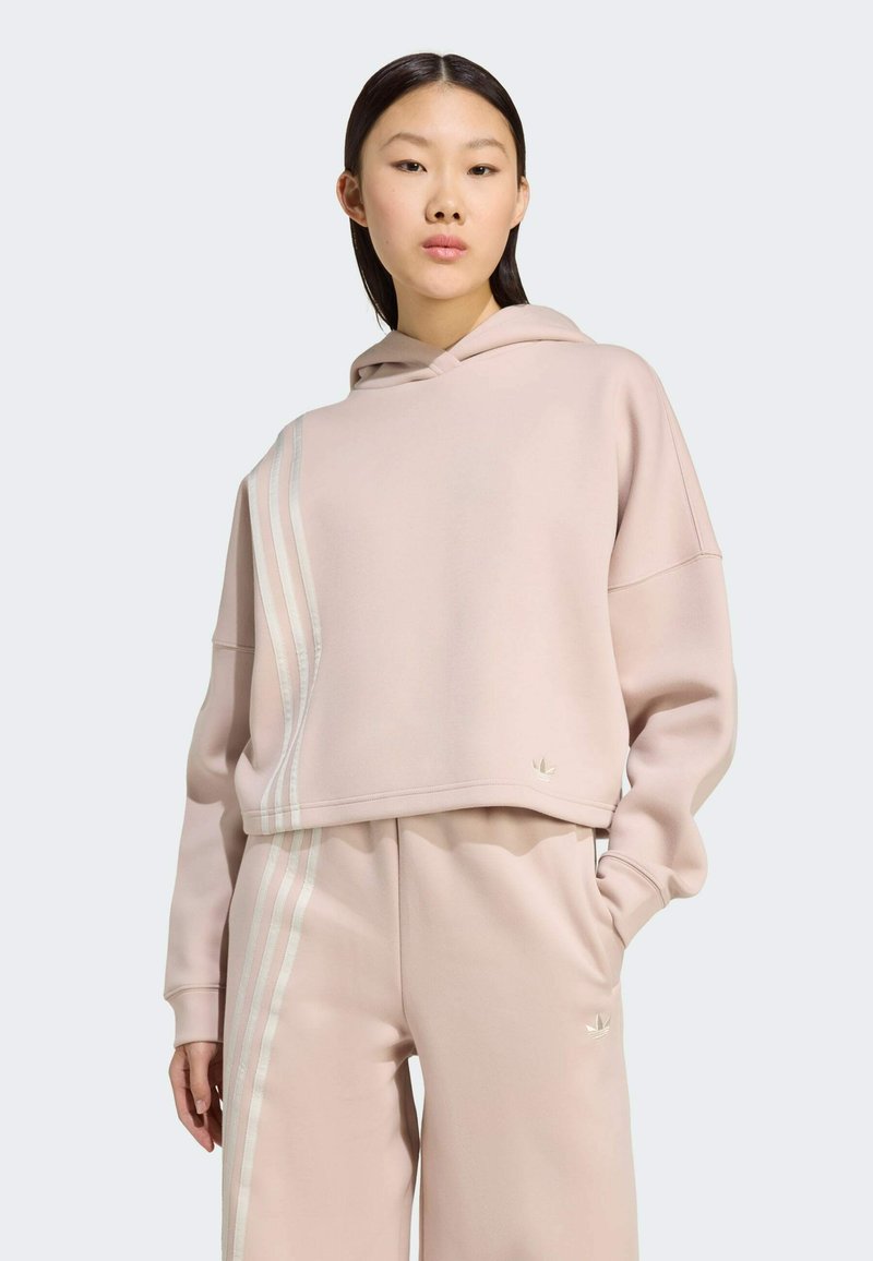 Pink cropped hoodie with a hood, featuring three white stripes on one side and a small logo on the hem. Soft texture and relaxed fit.