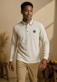 Lange mouwen crème polo shirt met een contrasterende kraag en logo patch, gecombineerd met beige broek. Heeft een gestructureerde stof en gekleurde accenten.