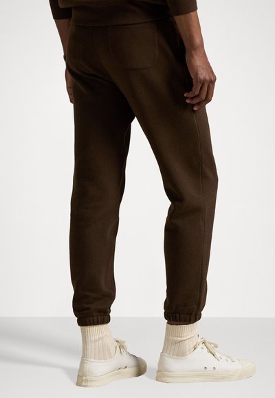 Brune sweatshirtbukser med en glat tekstur, elastiske manchetter og en baglomme. Parret med hvide sneakers og ribbede sokker i cremfarge.