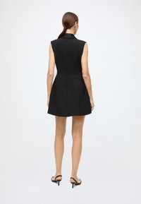 Black sleeveless dress with a tailored fit, flared skirt, and a collar. Smooth texture with vertical pleats at the back, paired with black heels.