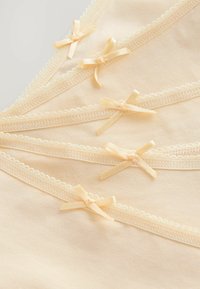 Miękka brzoskwiniowa tkanina z delikatną koronkową lamówką, ozdobiona małymi satynowymi kokardkami równomiernie rozmieszczonymi. Gładka tekstura i zaokrąglony dekolt.