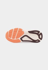 Zool van een sportschoen met een witte basis, oranje profiel aan de voorkant en bruine textuurgripsecties op een lichtgrijze achtergrond.