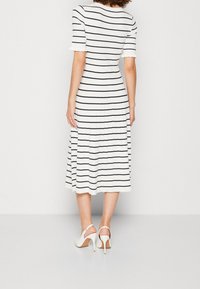 Weißes Midi-Kleid mit navyblauen horizontalen Streifen, kurzen Ärmeln und plissiertem Rock. Getragen mit weißen High-Heels mit Slingback.