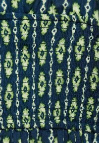 Tessuto di cotone con uno sfondo blu scuro e un motivo floreale e geometrico verde, che presenta un aspetto texturizzato e spiegazzato.