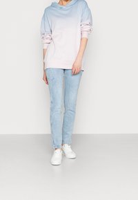 Sudadera ligera con ombré en azul y rosa, con un corte holgado y un bolsillo tipo canguro. Combinada con jeans ajustados de un azul claro y zapatillas blancas.