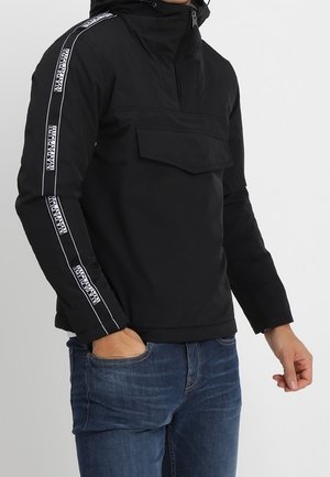 Mann trägt schwarzen Pullover mit Fronttasche und "NAPAPIJRI" Logo-Streifen an den Ärmeln, kombiniert mit blauer Jeans.