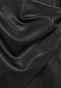 Tissu en cuir noir lisse avec des plis délicats et un léger éclat, montrant la texture et le tombé.