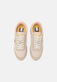 Baskets beiges avec une tige en maille et en daim, lacets blancs, accents roses et intérieur jaune avec une étiquette de logo. Semelle en caoutchouc texturée.