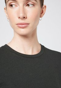 Sötétzöld, rövid ujjú környakú póló puha anyagból, amely sima textúrával és klasszikus szabással rendelkezik a nyak körül és a vállaknál.