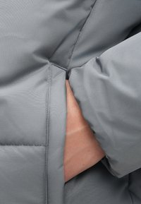 Hallide hall suvekate, millel on küljetasku ja käsi sees. Kanga tekstuur on sile ja õmblused on nähtavad õmbluste ümber.