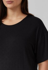 Czarny krótki top z krótkim rękawem z miękkiego materiału, z dekoltem w serek i subtelnymi błyszczącymi ozdobami. Luźny krój z obniżonymi ramionami.