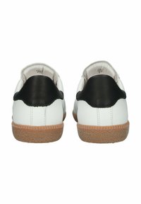 Valkoiset nahkakengät mustilla kantakohdilla ja tekstuurilla varustetulla ruskealla kumipohjalla, joissa on yksinkertainen muotoilu ja sileä pinta.