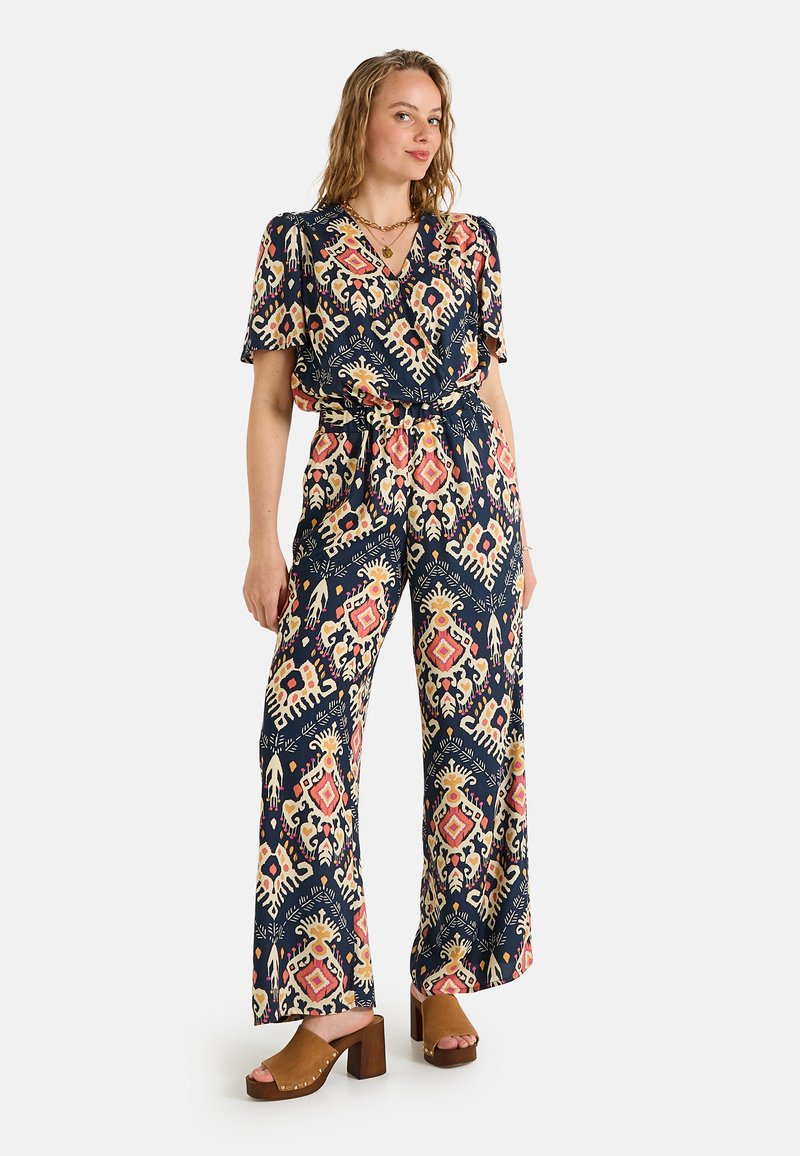 Combinaison à motifs avec manches courtes, fond bleu marine, designs floraux et géométriques vifs en rose et jaune, taille cintrée, jambes larges.