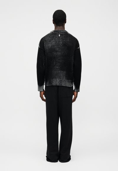 Μαύρο ριμπ πουλόβερ με στρογγυλή λαιμόκοψη, με ασημένια λεπτομέρεια και υφή, συνδυασμένο με μαύρο παντελόνι σε άνετη γραμμή.