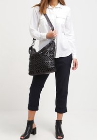 Musta nahkainen käsilaukku, jossa on leikatut kuviot, olkahihna ja hopeanväriset metalliosat. Yhdistetty valkoiseen paitaan ja laivastonsinisiin raitahousuihin.