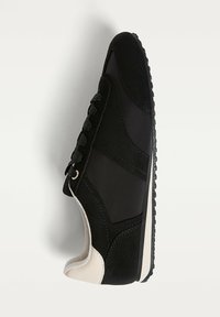 Baskets noires avec des panneaux en daim et en tissu, lacets noirs et un onglet de talon blanc sur fond blanc.