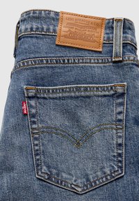 Poche arrière d’un jean Levi’s bleu avec coutures jaunes, étiquette rouge Levi’s et étiquette en cuir beige Levi Strauss & Co. sur la ceinture.