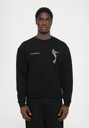 Sweatshirt noir en mélange de coton doux, avec un imprimé graphique et le texte "Unis par le rythme" sur le devant, avec des poignets côtelés.