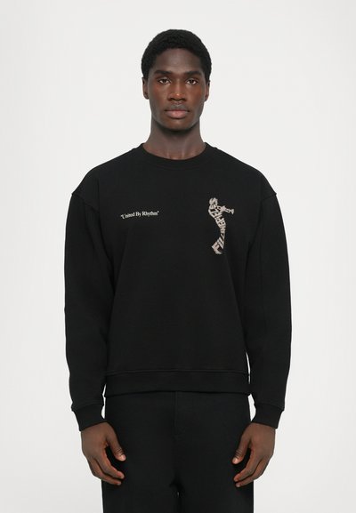 Sort sweatshirt lavet af blød bomuldsblanding, med et grafisk print og teksten "United By Rhythm" på forsiden, samt ribbede manchetter.