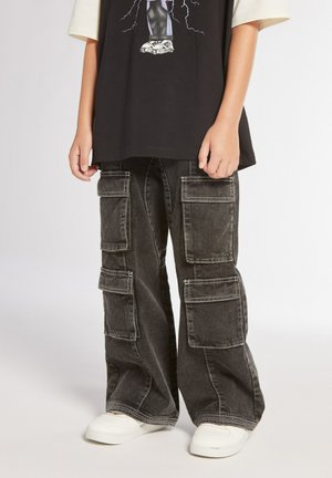 Pantaloni cargo neri con più tasche laterali, vestibilità ampia e cuciture a contrasto. Indossati con una maglietta nera con graphic e sneakers bianche.