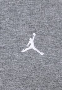 Szürke szövet, amelyen egy fehér jumpman logó látható, amely egy ugrásban lévő alakot ábrázol, hangsúlyozva a lágy érzetet és a sima textúrát.