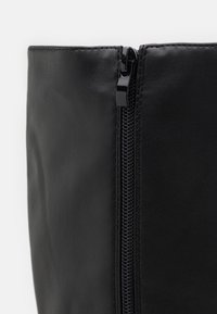 Černé kožené vysoké boty s předním zipem, texturovaným povrchem a čistými liniemi. Stahovák zipu je lesklý, což zvyšuje moderní design.