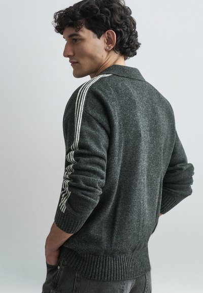Pull en maille gris foncé avec col, présentant des rayures blanches le long des manches et des bords-côtes aux poignets et à l'ourlet. Texture lisse, design décontracté.