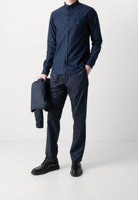 Marinblå skjorta med knappar och en liten broderad detalj, i kombination med matchande marinblå byxor och svarta skor; slätt tyg, avslappnad passform.