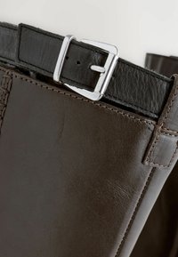 Cintura in pelle marrone con fibbia in metallo argentato, caratterizzata da cuciture dettagliate lungo i bordi e una superficie liscia.