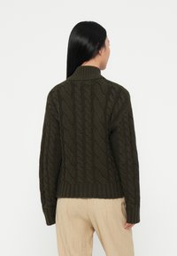 Dunkelgrüner Kabelstrickpullover mit hohem Kragen, geripptem Saum und langen Ärmeln, der über strukturierte Muster und eine lässige Passform verfügt.