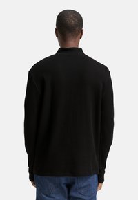 Schwarzes, geripptes Langarmshirt mit lockerem Sitz, flachem Kragen und glatter Textur, kombiniert mit blauen Jeans.