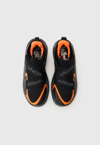 Pantofi sport negri cu accente portocalii, având un material textil texturat, detalii cu curea și brand vizibil pe lateral.