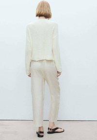 Krämfärgad stickad tröja med avslappnad passform, tillsammans med ljusbeiga linbyxor. Bruna flata sandaler med spänne fulländar outfiten.