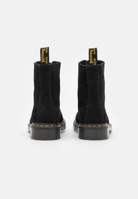 Black suede ankle boots with yellow pull tabs, contrasting yellow stitching, and chunky black rubber soles. Simple design, no additional embellishments.
