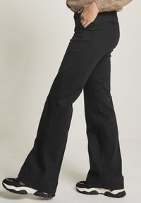 Svarta utsvängda byxor av denim med en klassisk passform och subtila sömnadsdetaljer. Kombinerade med svartvita sneakers.