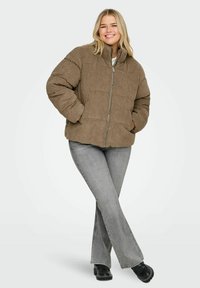 Smeđa pufasta jakna od korduroga s visokim ovratnikom, prednjim patentnim zatvaračem i bočnim džepovima; nošena preko sivih trapez hlača i crnih cipelama na platformu.