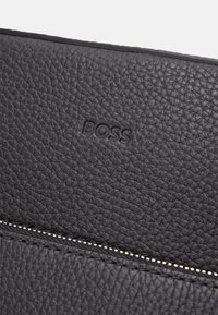 Czarny skórzany portfel o teksturowanej powierzchni z wytłoczonym logo "BOSS" oraz kontrastowym zamkiem błyskawicznym ze szwem.