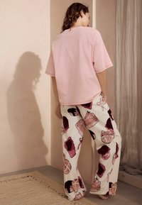 Lyserød oversized bomulds t-shirt med korte ærmer og hvide pyjamasbukser med farverige dessertmønstre, står på en struktureret overflade.
