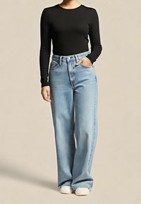 Osoba nosící černý top s dlouhými rukávy, světle modré široké džíny s vysokým pasem, jednu ruku má v kapse, a bílé tenisky.