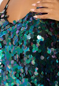 Paljetttopp med reflekterande, iriserande cirkulära paljetter i nyanser av grönt och blått, lager på lager på svart nätmaterial.