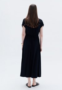 Abito nero al ginocchio in morbido tessuto con maniche corte e vita cinchata. Abbinato a sandali neri. Design semplice e fluido.