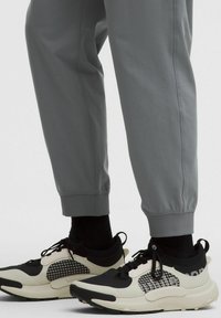 Graue Jogginghosen mit gerippten Bündchen, kombiniert mit schwarz-weißen Sneakern mit strukturiertem Muster und Schnürsenkeln. Schwarze Socken sichtbar.