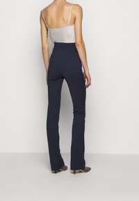 Pantalones de tiro alto en navy con un corte ajustado, hechos de una tela suave. El conjunto incluye una blusa de tirantes de satén ligero.