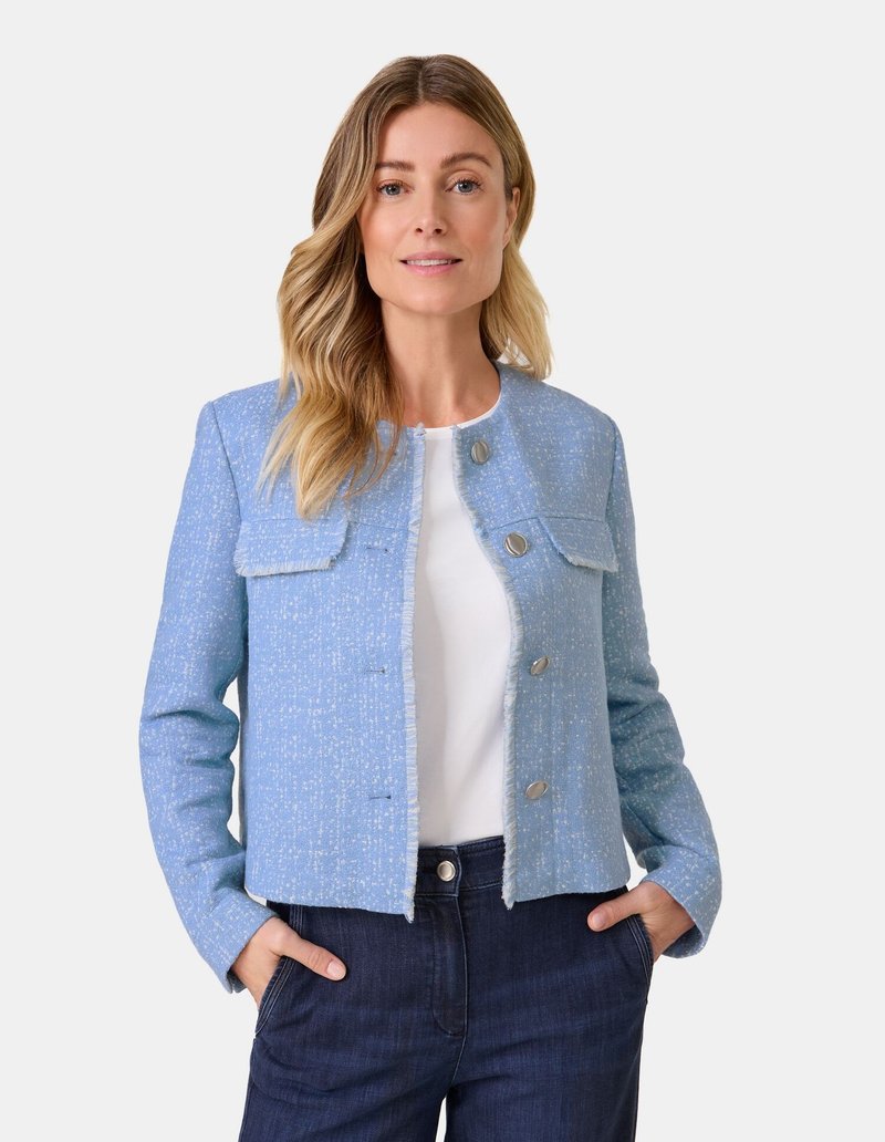 Hellblaue Boucle-Jacke mit fransigen Kanten, zwei Fronttaschen und silbernen Knöpfen. Getragen über einem weißen Oberteil und kombiniert mit dunkelblauen Jeans.