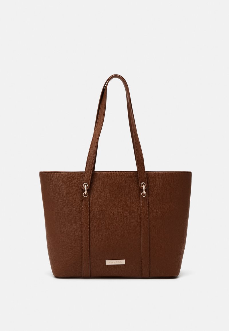Bolsa de tote texturizada castanha com alças duplas, apresentando detalhes metálicos e uma placa de marca discreta na parte da frente.