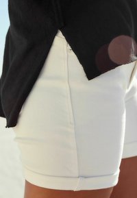 Witte denim korte broek met een strakke pasvorm en opgerolde hems, gecombineerd met een zwart top met een licht rafelige rand. Buiten achtergrond.