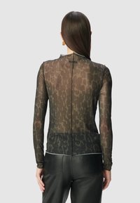 Top nero trasparente a maniche lunghe con stampa leopardata testurizzata, colletto alto e chiusura con zip sulla schiena. Abbinato a pantaloni in finta pelle nera.