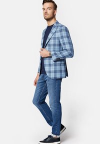 Jasnoniebieska marynarka w kratę z pojedynczym zapięciem na guzik, zestawiona z granatową koszulą, dżinsami oraz ciemnymi trampkami.