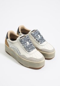 Zapatillas de cuero blancas con una puntera y laterales de ante gris, que cuentan con cordones texturizados a rayas en blanco y negro, y un acento metálico plateado.